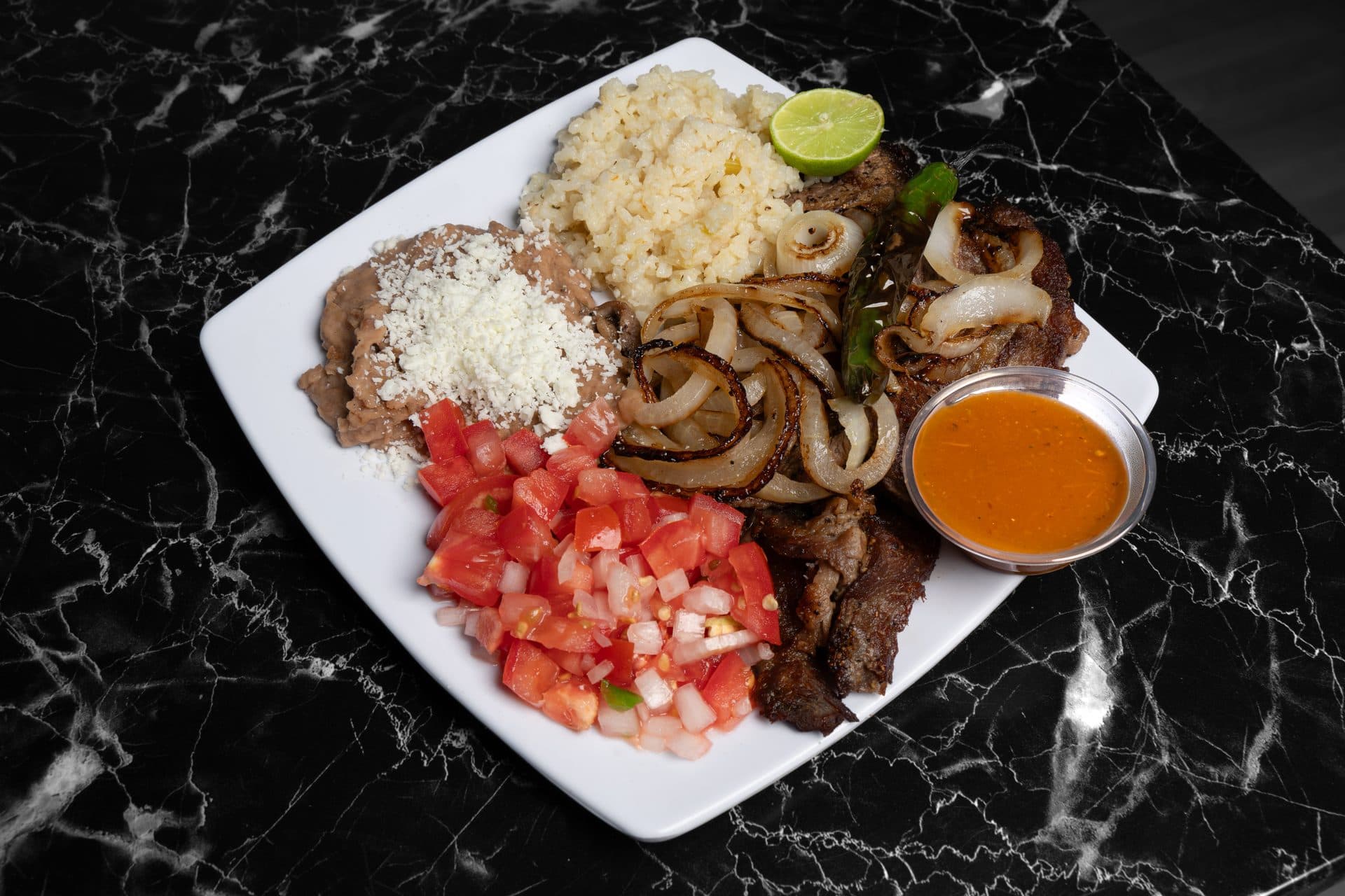 Plato de carne asada con cebolla, frijoles, arroz y queso